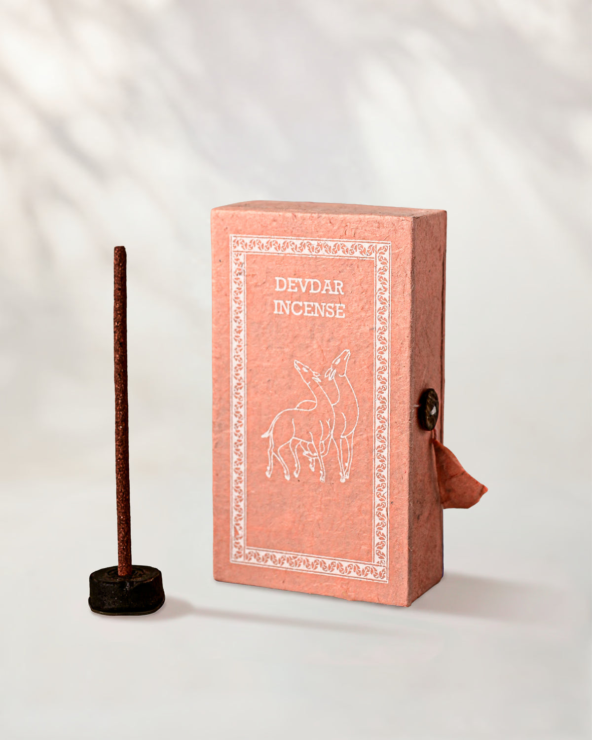 Devdar Stupa Incense Sticks, box of 40: pink handmade paper box with a deer motif beside one stick in a small holder.