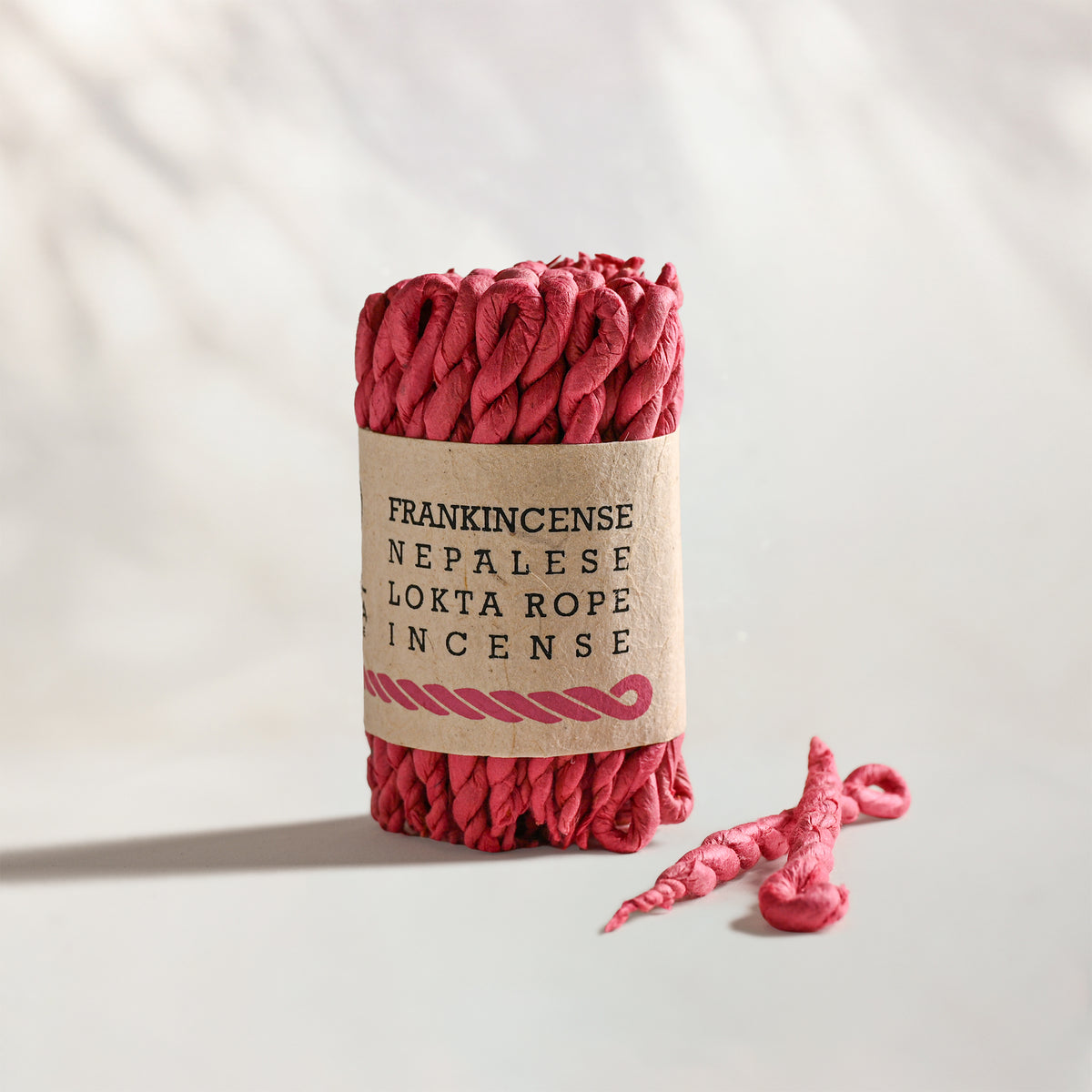 Frankincense Lokta Rope Incense Bundle: red twisted rope incense in a kraft paper band, two loose ropes beside it.
