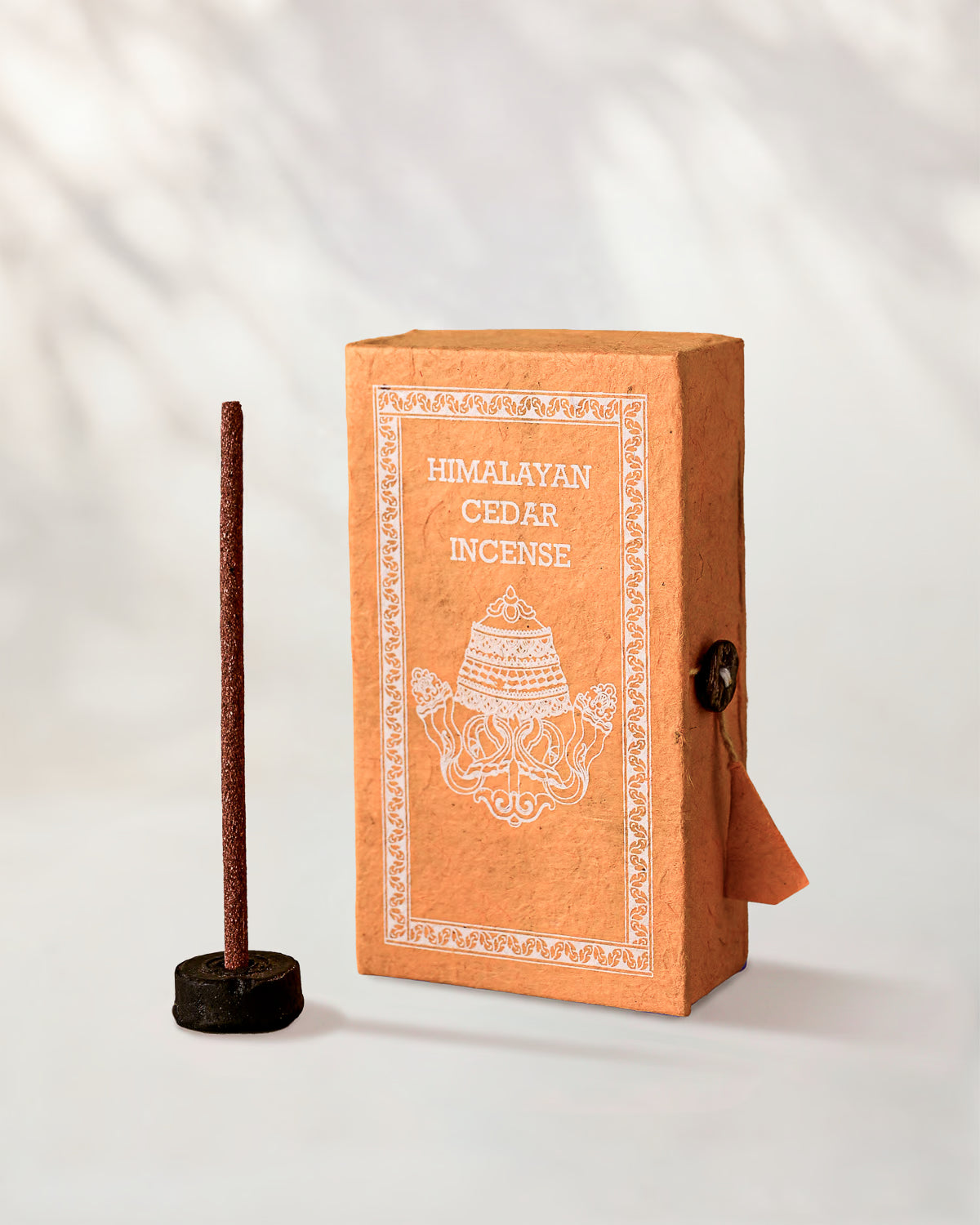 Himalayan Cedar Incense Sticks, box of 40: orange Stupa paper box with white print beside a stick standing in a small holder.