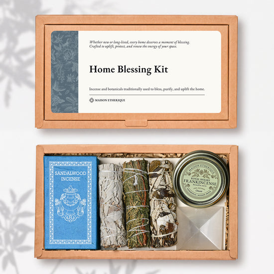 Home Blessing Kit: kraft box lid above the open box with sandalwood incense, three smudge sticks, a frankincense tin and a white crystal pyramid.