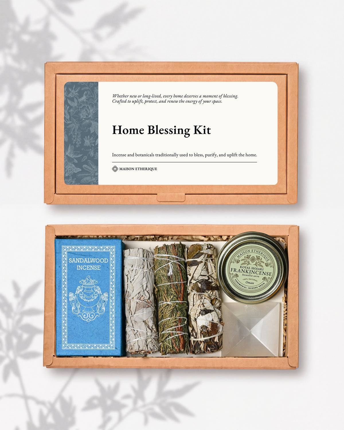 Home Blessing Kit: kraft box lid above the open box with sandalwood incense, three smudge sticks, a frankincense tin and a white crystal pyramid.