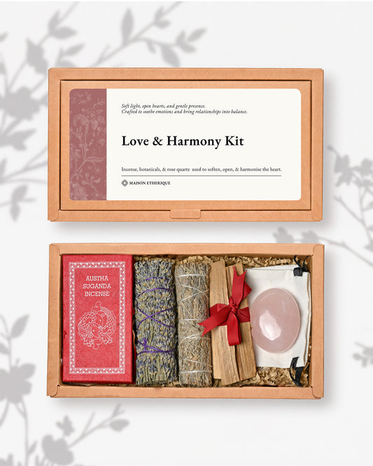 An open gift box labeled 'Love & Harmony Kit' containing a red incense packet, lavender and sage bundles, palo santo sticks, and a pink rose quartz crystal on a white background with a subtle leafy shadow overlay.
