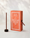 Na Swa Incense Sticks, box of 40: coral Stupa paper box with white print beside a stick standing in a small holder.
