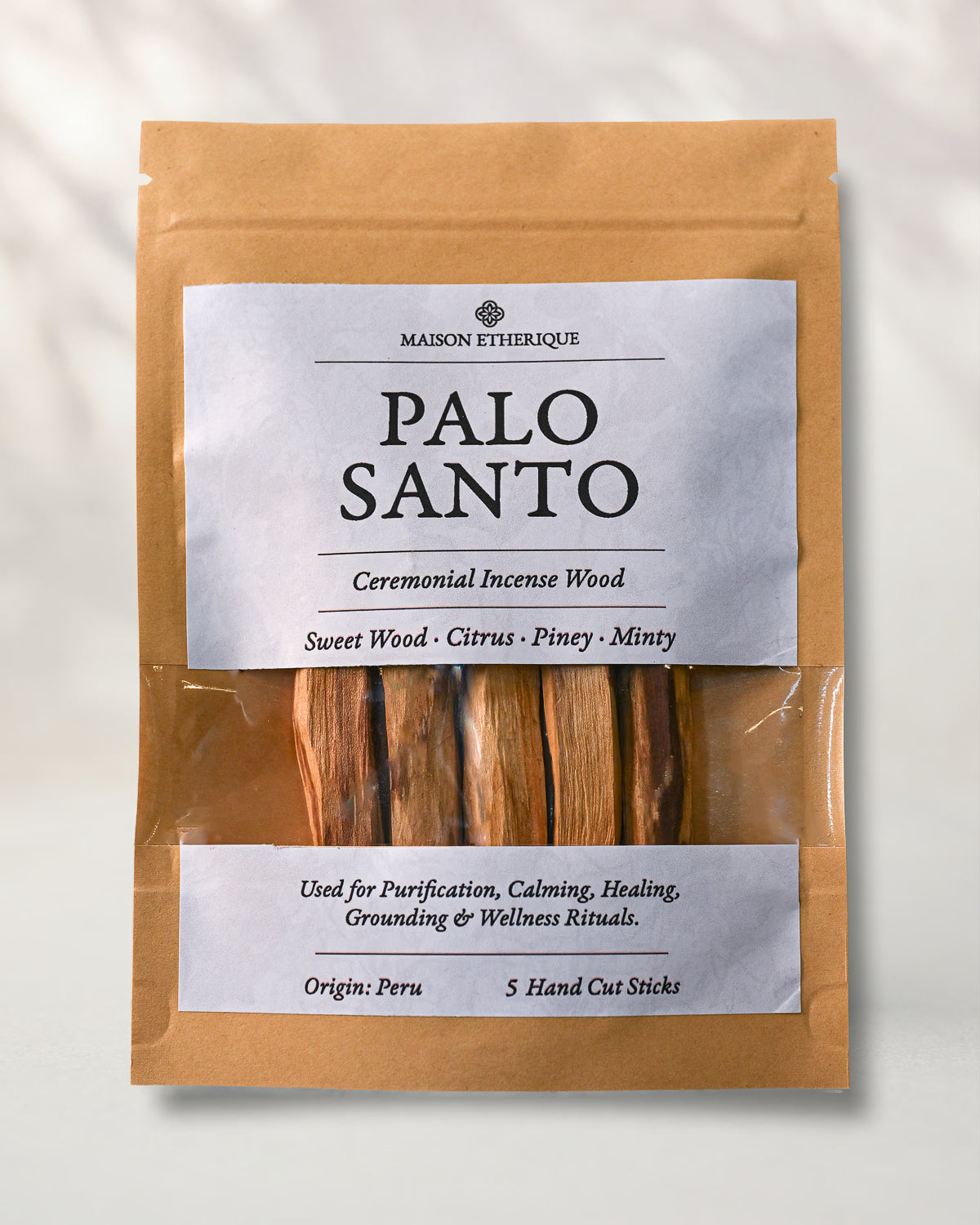 Front of a kraft pouch of Maison Éthérique Palo Santo, five hand-cut sticks visible through a clear window, on a pale background.