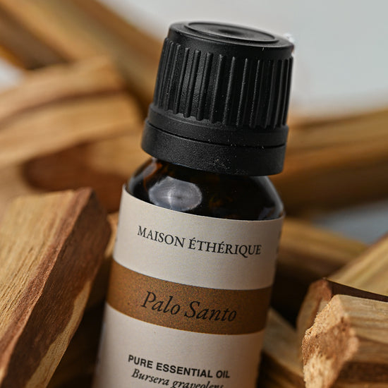 10 ml bottle of Maison Éthérique Palo Santo essential oil resting on Palo Santo sticks.