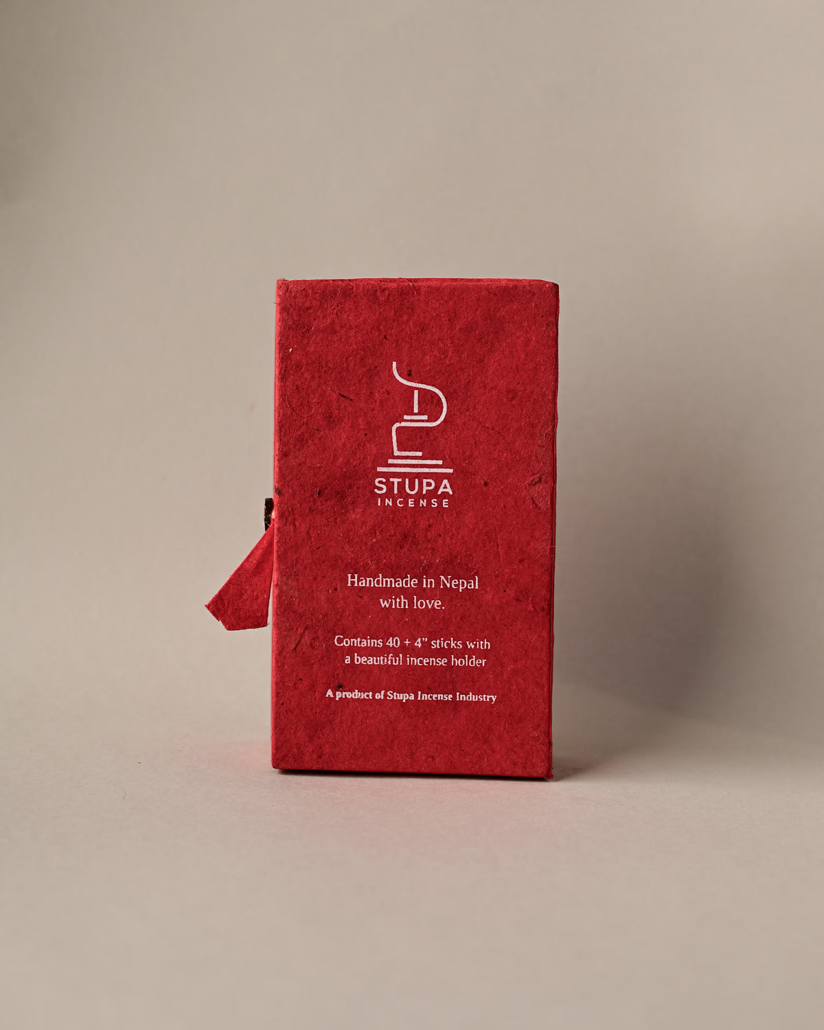 Back of a red paper box of Stupa Austha Suganda incense sticks, handmade in Nepal, on a pale background.