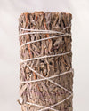 Blue sage smudge stick, dried blue sage leaves bound with white string, shown close against a pale background.