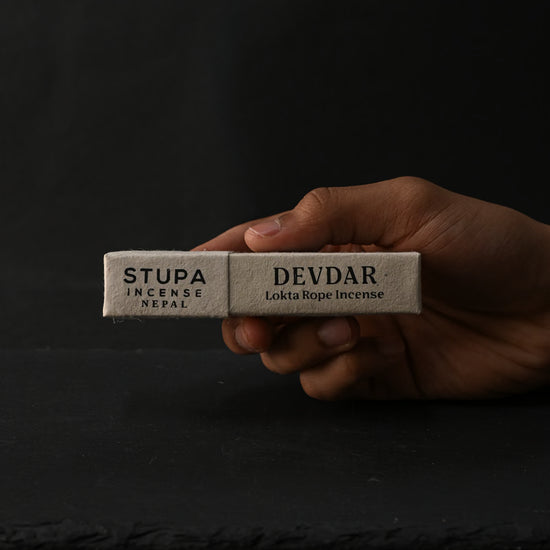 Hand holding a box of Stupa Devdar lokta rope incense against a dark background.