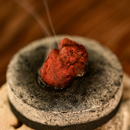 Dragon's Blood resin smouldering on a charcoal disc, a thin line of smoke rising.