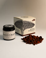 Amber jar and illustrated box of Maison Éthérique Dragon's Blood resin beside a small heap of deep red resin pieces.
