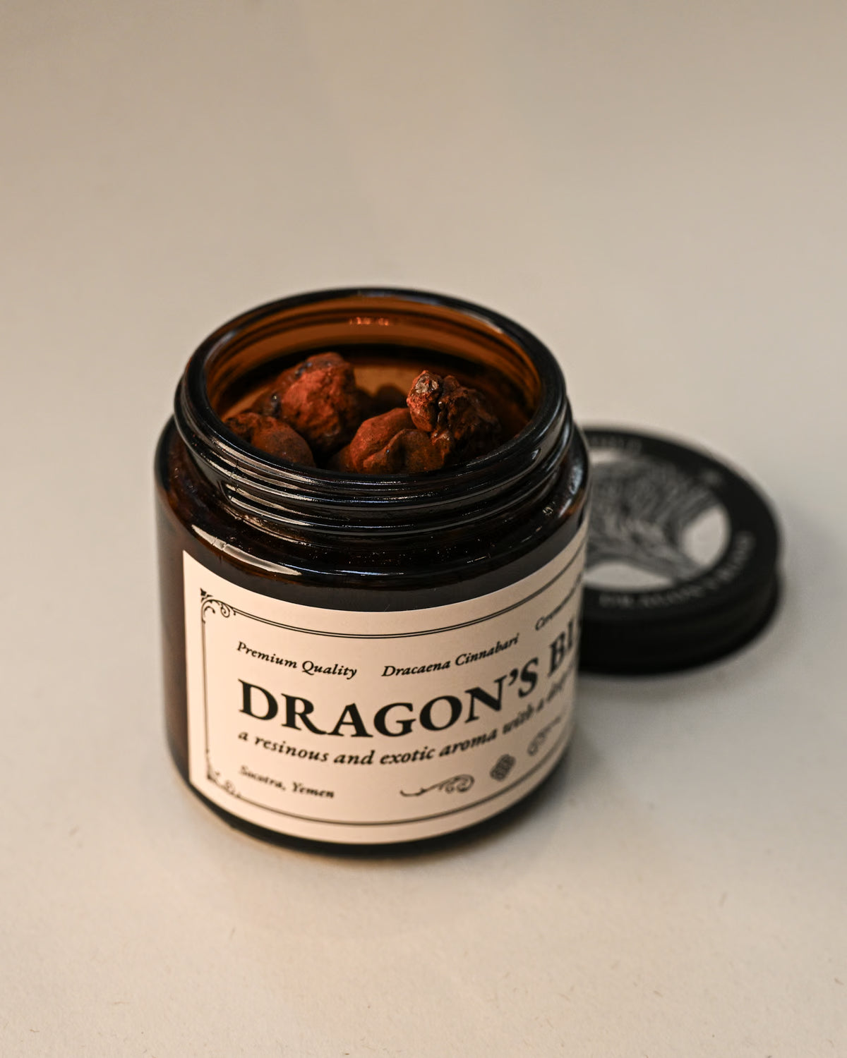 Open amber jar of Maison Éthérique Dragon's Blood resin with its lid beside it, on a pale background.