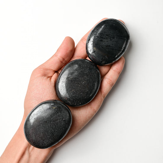 Three polished hematite palm stones resting in an open hand against a white background.