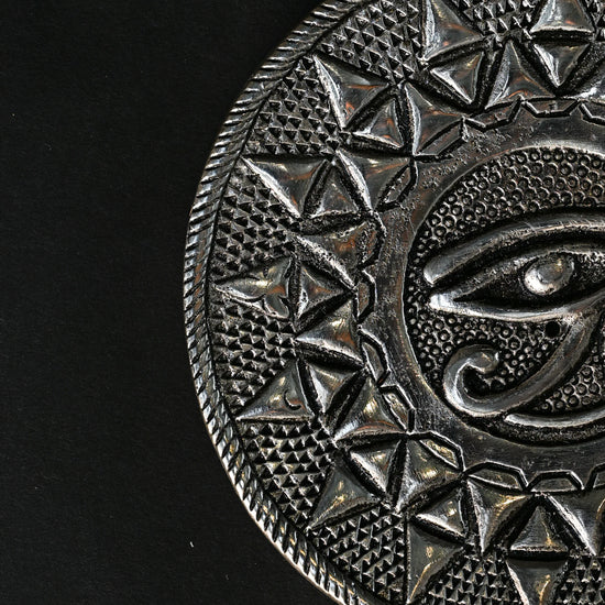 Close view of the Eye of Horus metal incense holder, showing the embossed eye and triangular border.