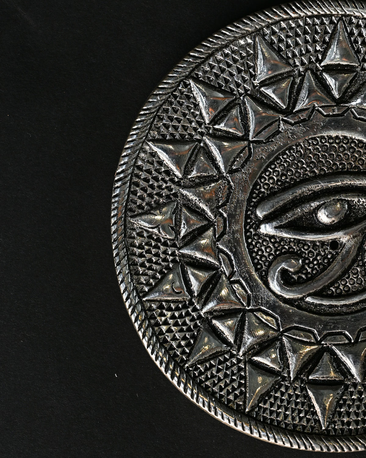 Close view of the Eye of Horus metal incense holder, showing the embossed eye and triangular border.