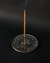 Incense stick standing upright in the Eye of Horus metal holder against a dark background.