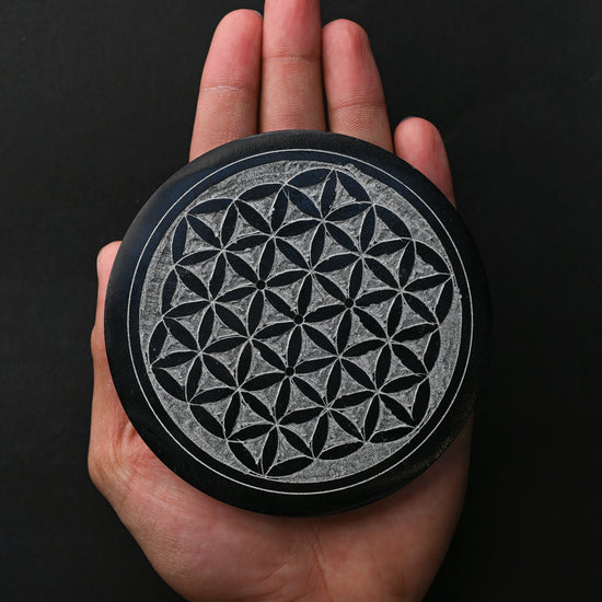 Round Flower of Life stone incense holder resting on an open palm.
