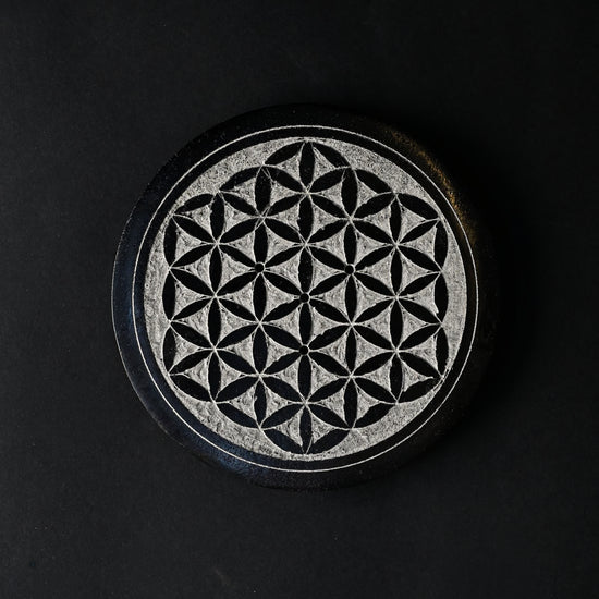Round stone incense stick holder carved with a Flower of Life pattern, seen from above on a dark background.