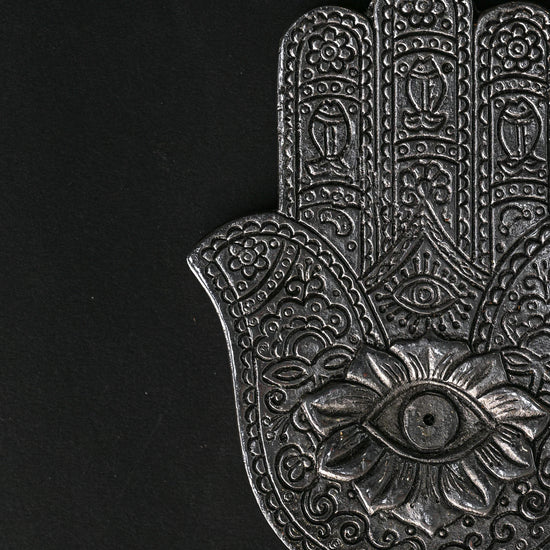 Close view of the hand-shaped metal incense holder, showing the embossed eye and floral detail.