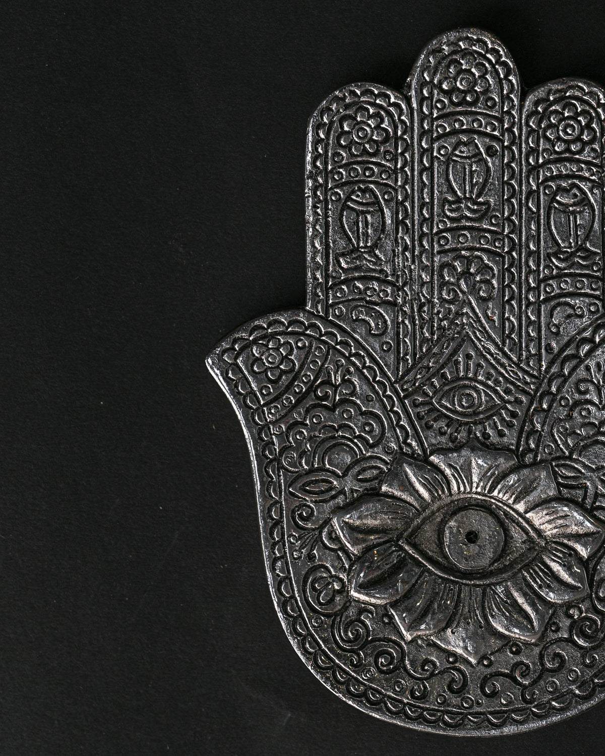 Close view of the hand-shaped metal incense holder, showing the embossed eye and floral detail.