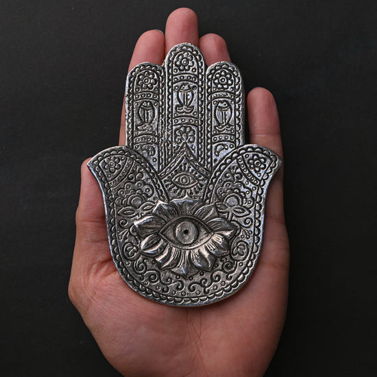 Hand-shaped metal incense holder with an eye motif resting on an open palm.
