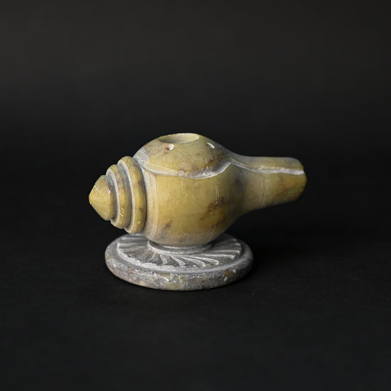 Shankh incense stick holder carved from green-yellow stone in the form of a conch, on a dark background.