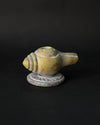 Shankh incense stick holder carved from green-yellow stone in the form of a conch, on a dark background.