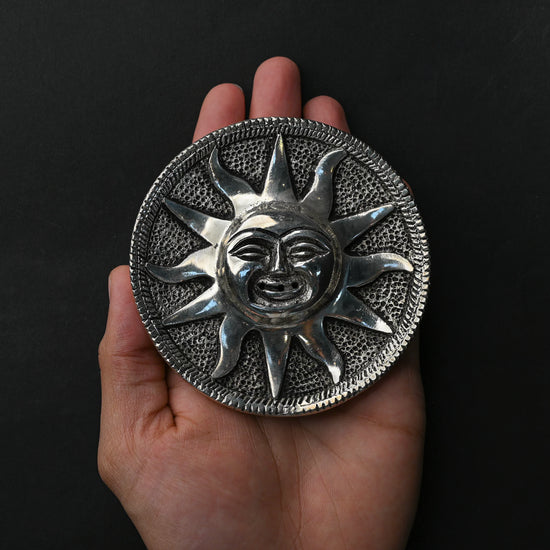 Surya sun-face metal incense holder resting on an open palm.