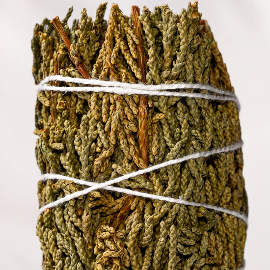 Juniper smudge stick, dried green juniper sprigs bound with white string, shown close against a pale background.