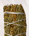 Juniper smudge stick, dried green juniper sprigs bound with white string, shown close against a pale background.