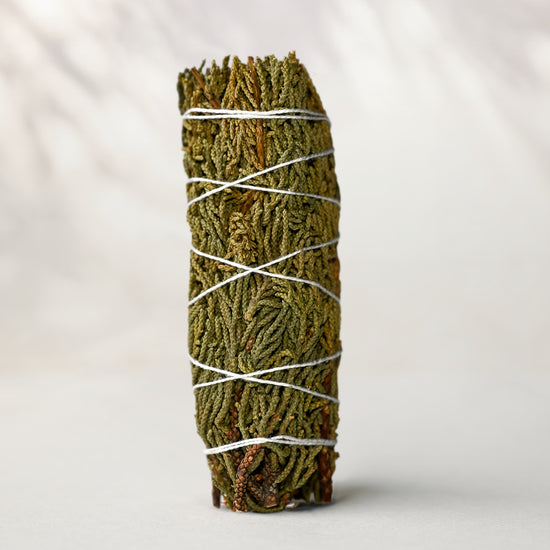 Juniper smudge stick standing upright, green juniper sprigs bound with white string, on a pale surface.