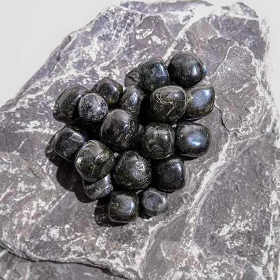 Polished black larvikite tumbled stones gathered on a slab of grey rock.