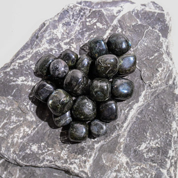 Polished black larvikite tumbled stones gathered on a slab of grey rock.
