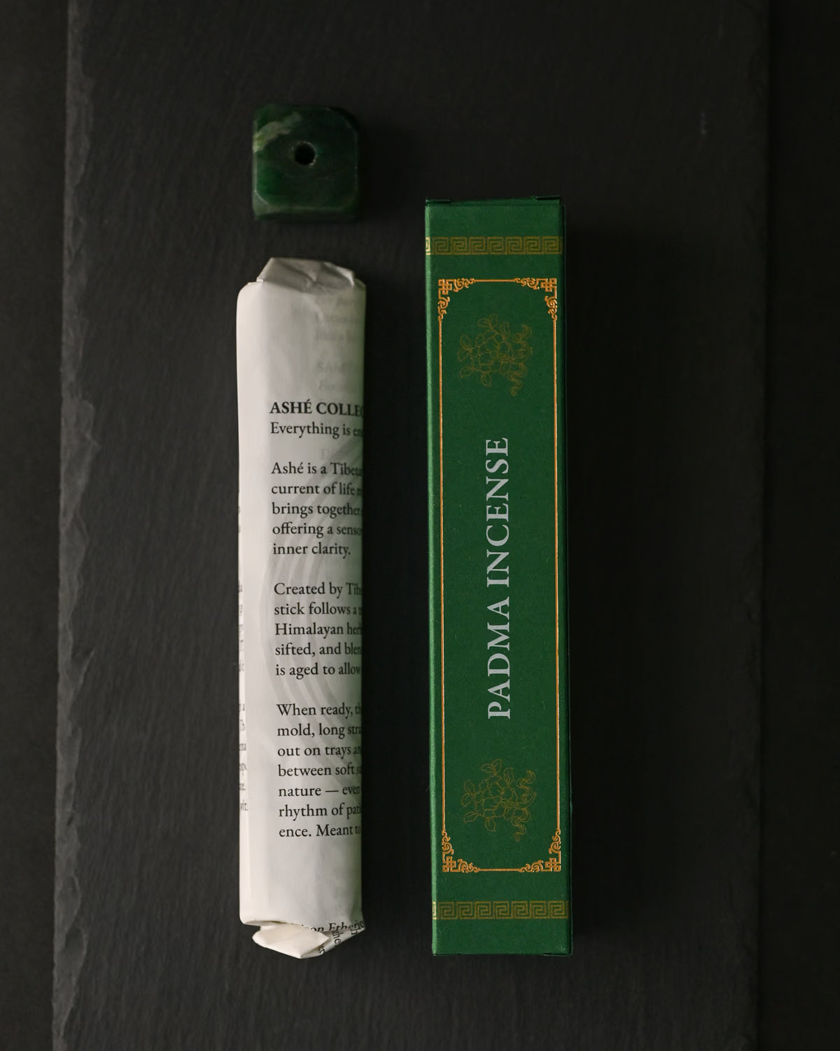 Padma Tibetan incense: paper-wrapped bundle, green box and small green holder laid out on dark slate.
