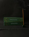 Two green boxes of Padma Tibetan incense beside a stick burning upright in a small green holder, on a dark background.