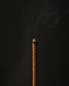 Close view of the glowing tip of a Padma Tibetan incense stick with a wisp of smoke.