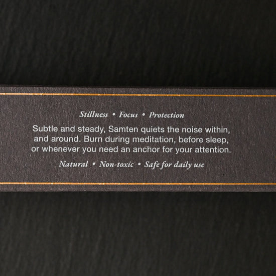 Side of the dark Samten Tibetan incense box with printed text and gold lines, on a dark background.