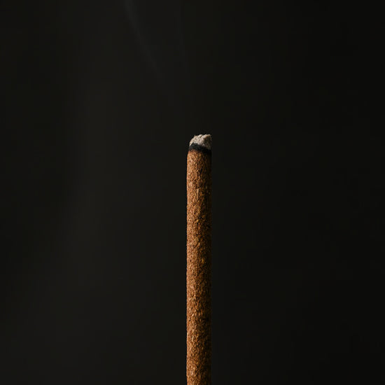 Close view of the tip of a Samten Tibetan incense stick with a wisp of smoke.