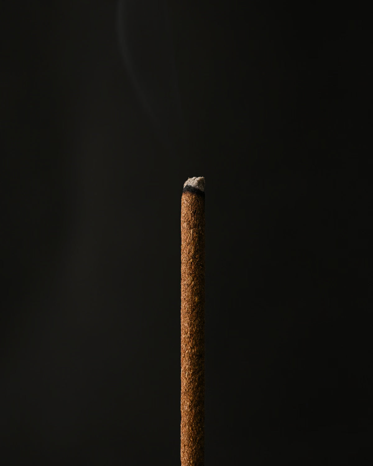 Close view of the tip of a Samten Tibetan incense stick with a wisp of smoke.