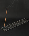 Incense stick burning at an angle in the 7 Chakra metal incense holder, a thin line of smoke rising.