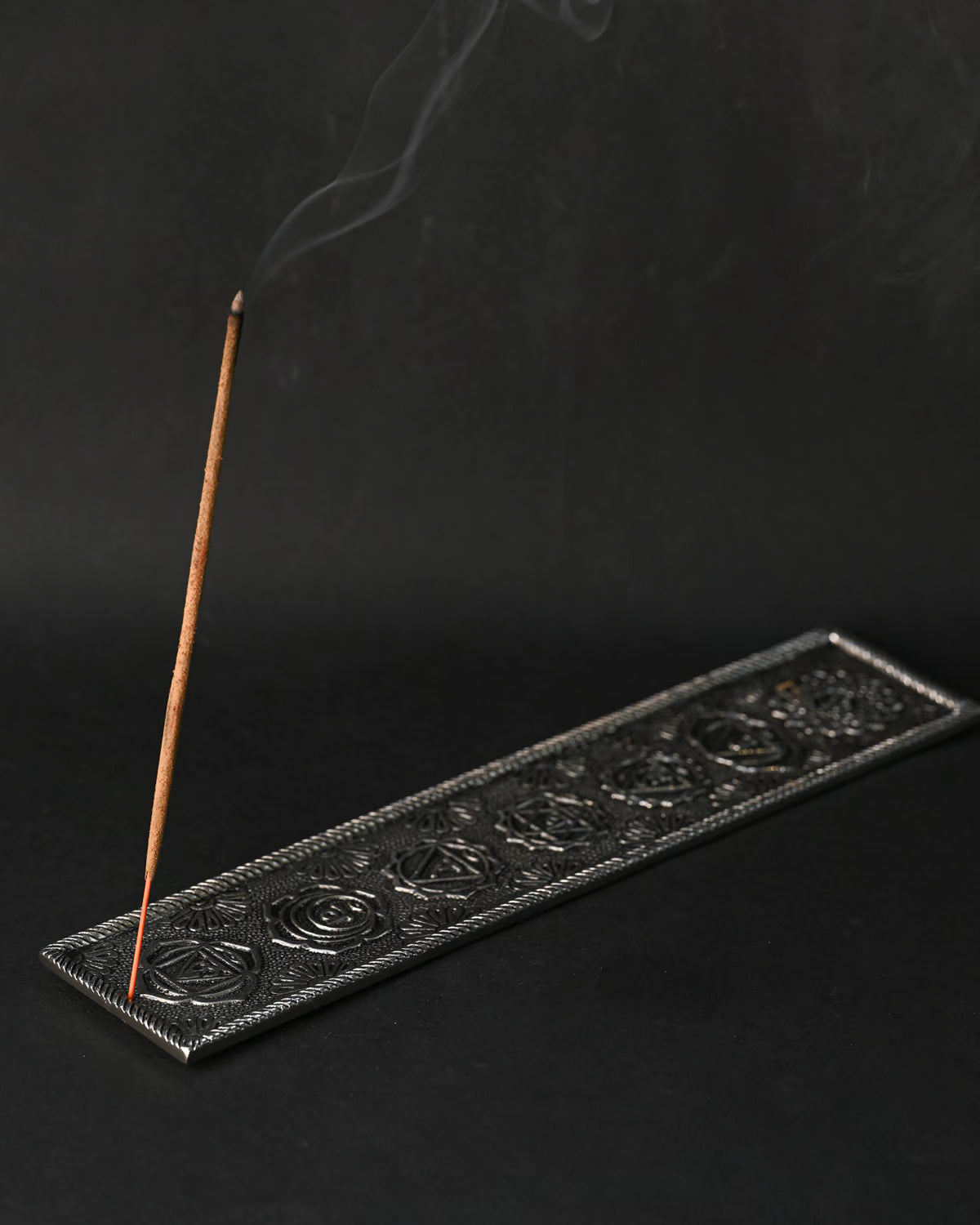 Incense stick burning at an angle in the 7 Chakra metal incense holder, a thin line of smoke rising.