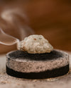 Piece of White Copal resin smouldering on a charcoal disc, smoke rising.