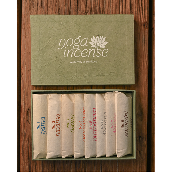 Yoga Incense gift box with its lid above and eight paper-wrapped incense bundles inside, on a wooden surface.