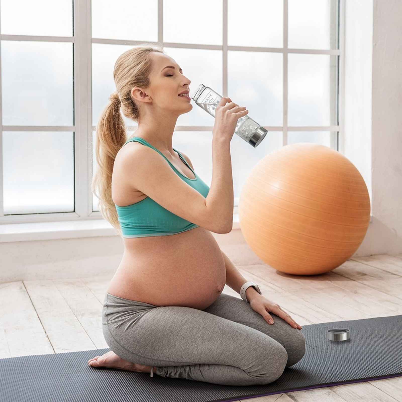 A pregnant woman drinking from a Tumbled Clear Quartz Crystal Water Bottle 